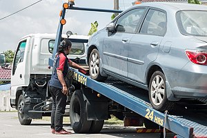 Man loading blue car onto tow truck