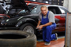 mature man car mechanician changing car wheel in auto repair shop