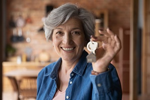 smiling mature woman holding key from new home wondering do landlords have to have insurance