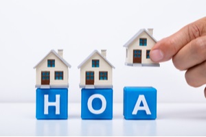 hand placing house model over red hoa blocks on wooden desk