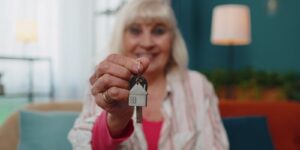 senior old woman customer landlord hold key to new house apartment give to camera