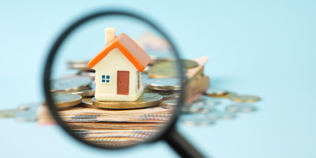 house and money under a magnifying glass