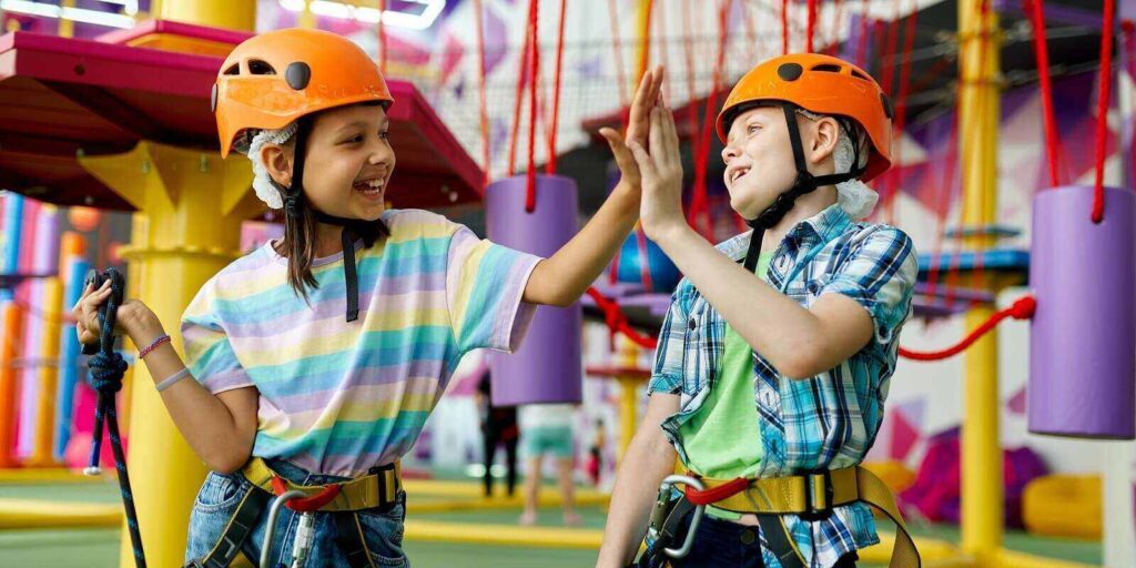two children in helmets climb on zip line