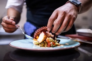 hands finishing plating the octopus for restaurant customers