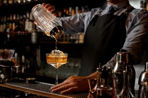 professional bartender in black apron pours drink from shaker into glass