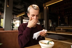 young man in a cafe covers his mouth with a hand disgusted with a taste of food