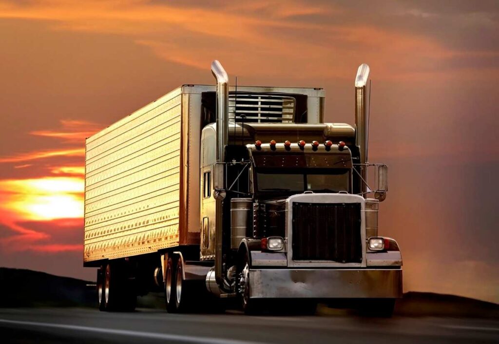 big truck driving on a highway with sunset in background