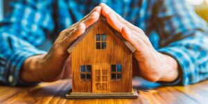 hands covering a model home, symbolizing home insurance and protection