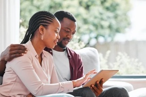 black couple and smile with tablet on sofa at home with browsing internet for house insurance options