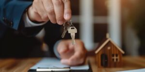 realtor handing house keys to happy homeowner with mortgage agreement at desk