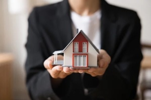 close up of female in formal jacket holds miniature of modern cottage house