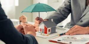 insurance agent's hand holds an umbrella over a small house