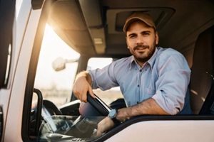 young truck driver behind steering wheel in vehicle cabin looking at camera