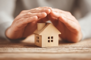 Hands Covering Small Wooden House Representing Home Insurance