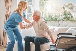 Assisted Living Employee Helping an Old Man to Get Out of Bed